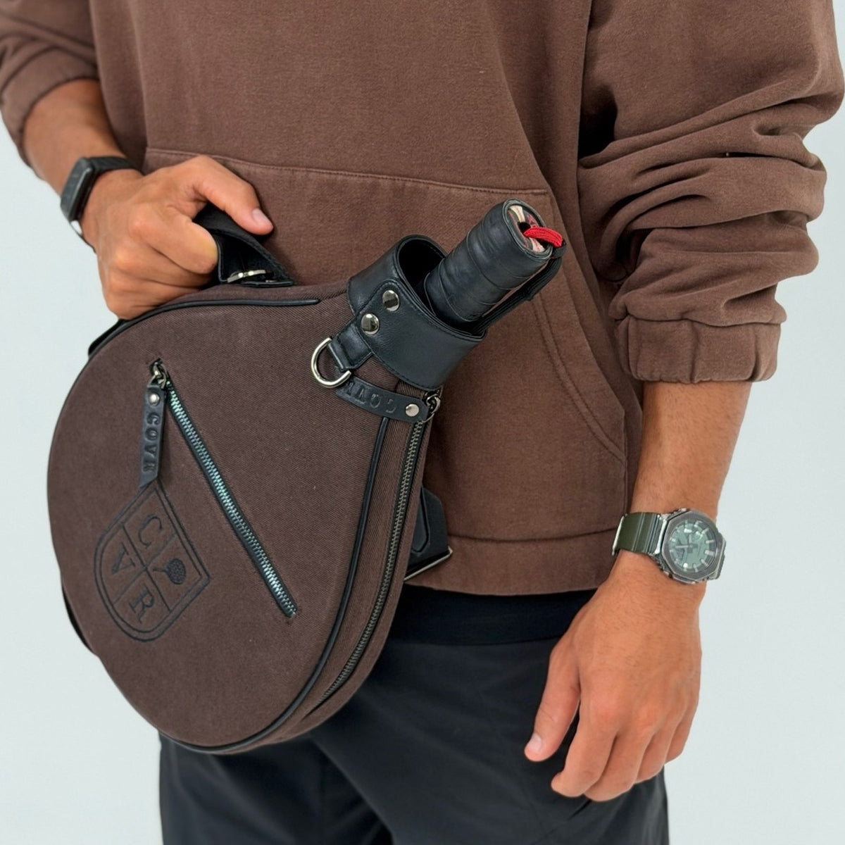 Player in a brown hoodie with a Coffee COVR padel racket cover
